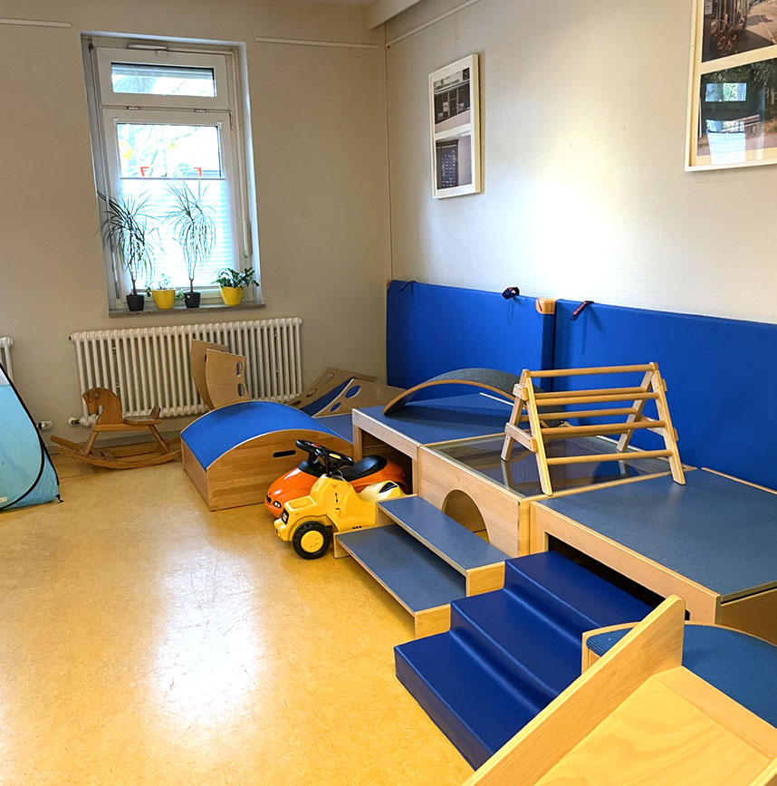 Spielbereich mit Holzgeräten, Rutsche, Kinderfahrzeug und Kletterbogen