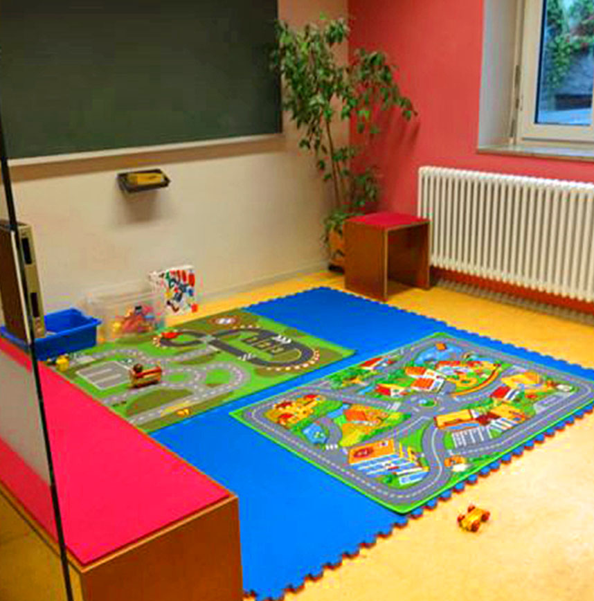 Spielecke mit bunten Straßenteppichen und Bausteinen vor einer Tafel