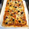 Rechteckige Pizza mit Gemüse und schwarzen Oliven