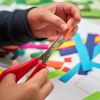 Kinderhände schneiden bunte Papierstreifen mit Schere