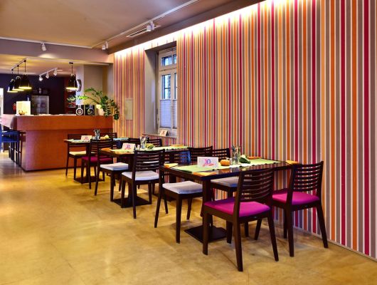 Ein hell beleuchteter Café-Raum mit Theke und Tischen und Stühlen vor einer gestreiften Wand.